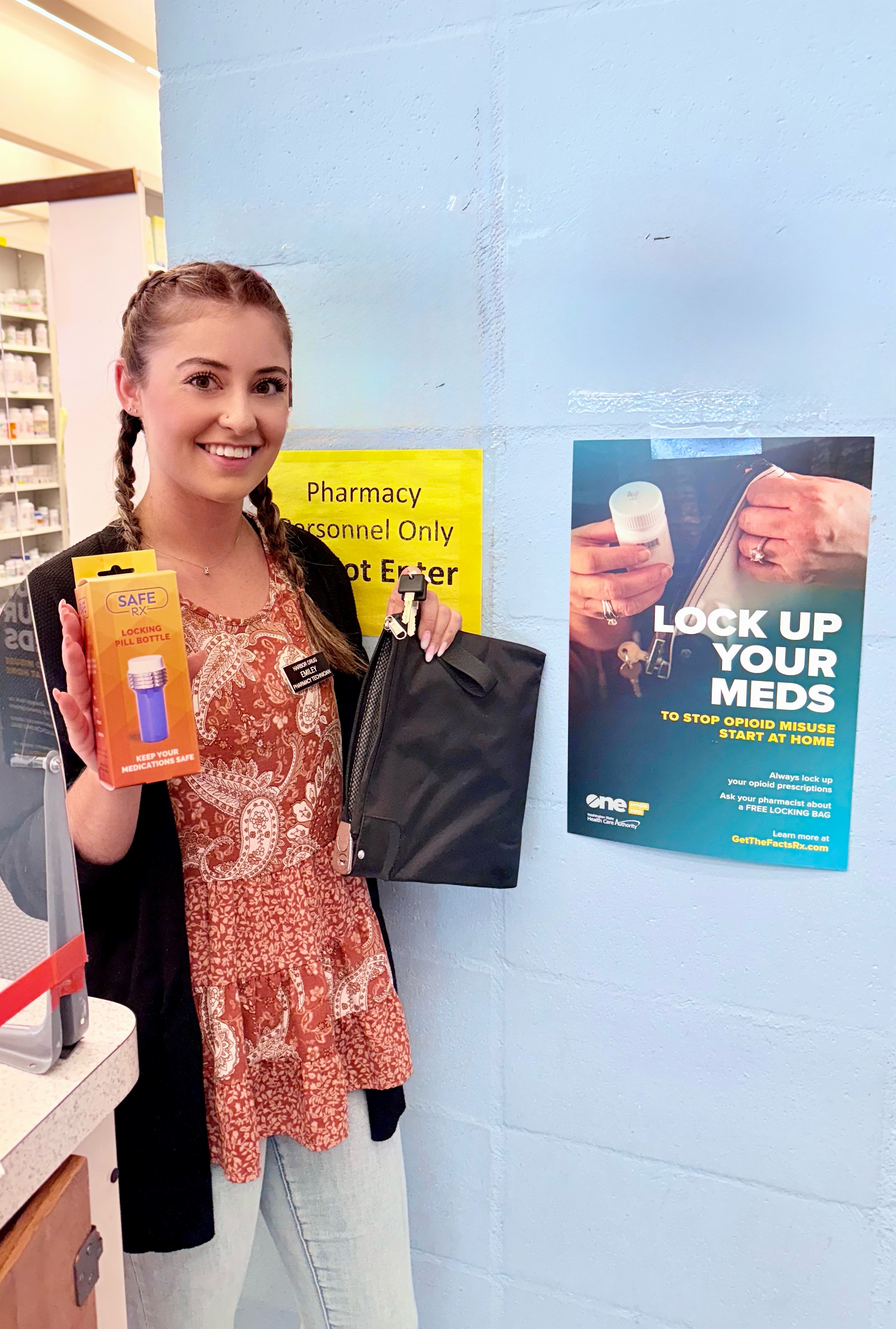 Pharmacist holding lock bag, standing next to campaign poster.
