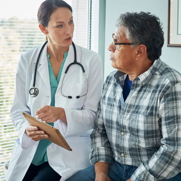 female doctor is talking to older male patient in a blue plaid shirt.