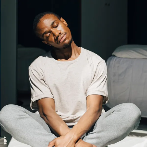 man meditates sitting criss cross in bedroom.