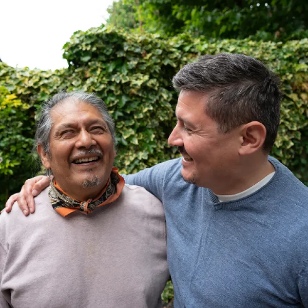 Middle age man in blue sweater smiles and has arm around older man wearing an oranged patterned neck tie